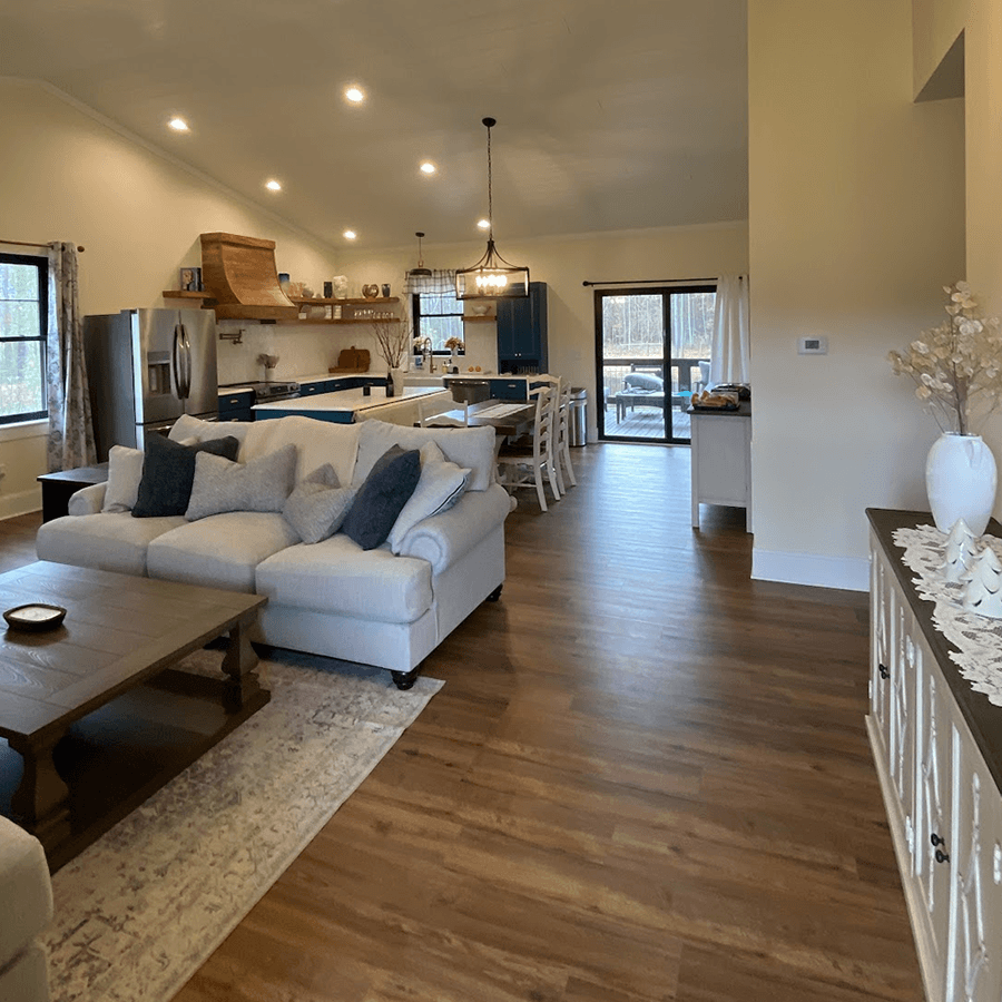 A spacious, modern living area features a cozy sectional sofa, a dining table, and a contemporary kitchen with blue cabinetry.