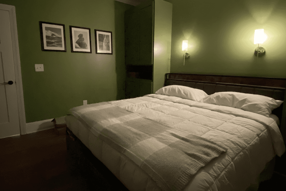 A cozy bedroom featuring a green wall, a bed with white linens, and framed pictures above.